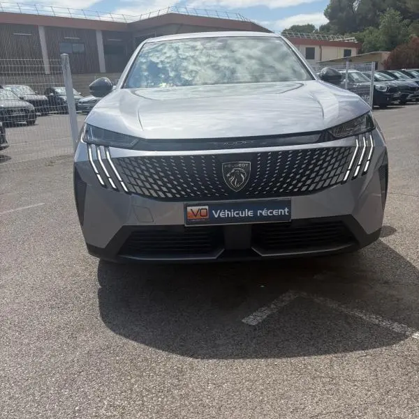 Vue frontale d'un Peugeot 3008 Hybrid gris clair 2025 avec calandre noire et feux LED distinctifs en forme de griffes.