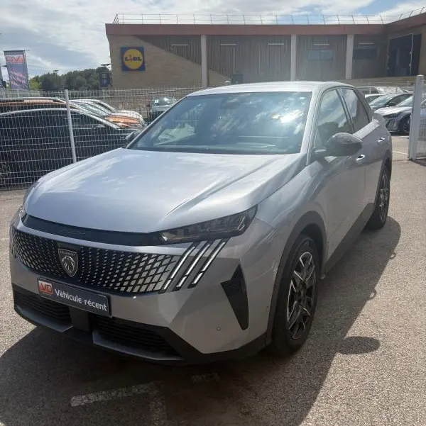 Vue 3/4 avant d'un Peugeot 3008 Hybrid gris clair 2025 avec calandre distinctive et feux LED verticaux.