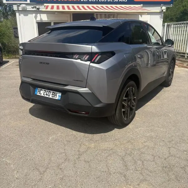 Vue 3/4 arrière droite d’un Peugeot 3008 Hybrid gris clair 2025 avec feux arrière distinctifs et toit noir.