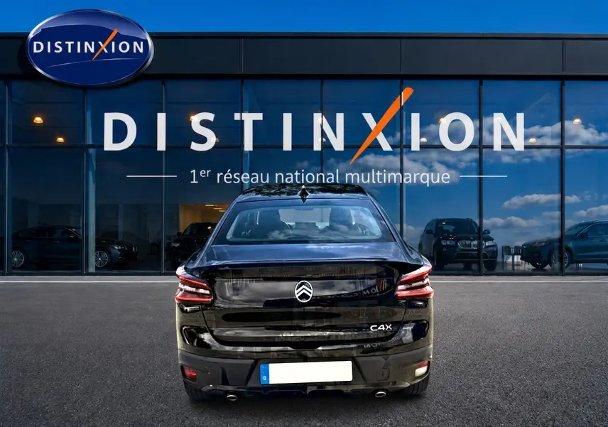 Vue arrière d'une Citroën C4 X noire 2025, avec feux LED et double sortie d'échappement visible devant une vitrine Distinxion.