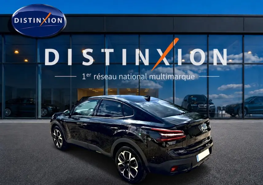 Vue 3/4 arrière droite d'une Citroën C4 X noire 2025, avec jantes alu et feux arrière LED, devant un showroom Distinxion.
