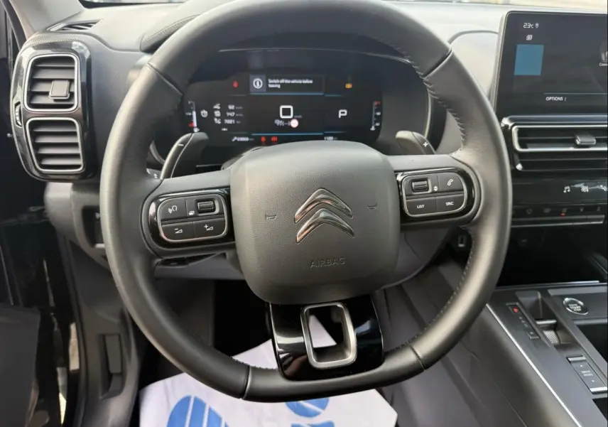 Vue intérieure centrée sur le volant noir du Citroën C5 Aircross 2024 avec tableau de bord numérique et console moderne.