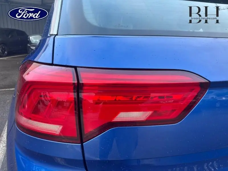 Gros plan sur le feu arrière gauche rouge du Volkswagen T-Roc bleu Ravenna métallisé, avec partie de la lunette arrière visible.