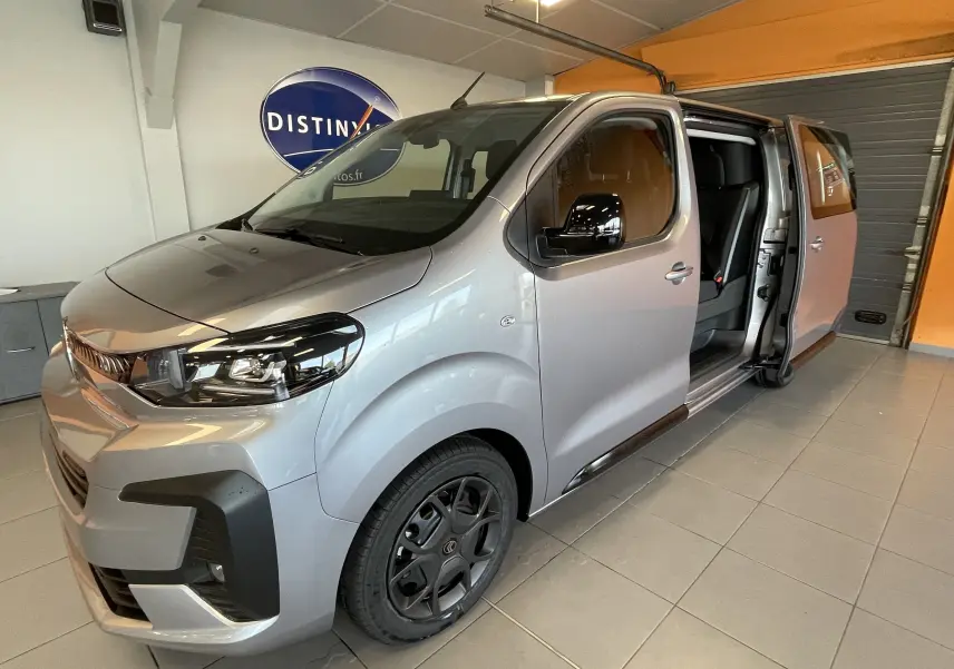 Vue 3/4 avant droit du Citroën Jumpy gris Artense avec porte latérale coulissante ouverte en intérieur showroom.