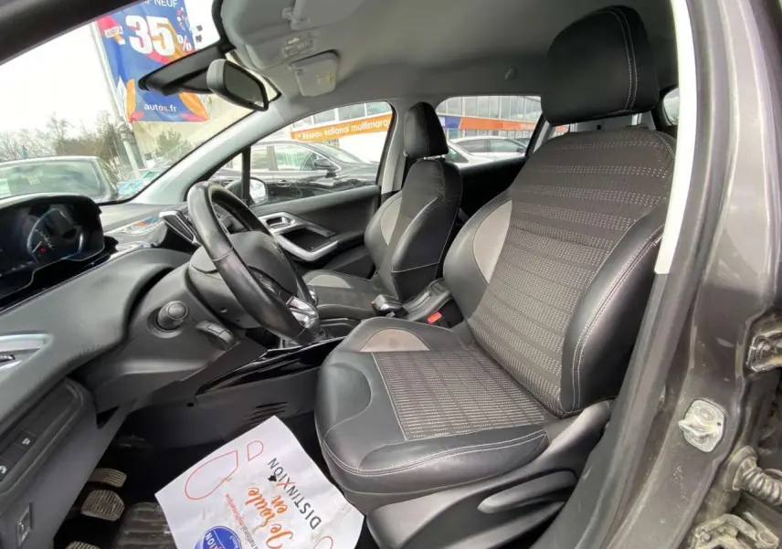 Vue intérieure côté conducteur de la Peugeot 2008 gris platinium, montrant sièges et volant noir avec tableau de bord moderne.