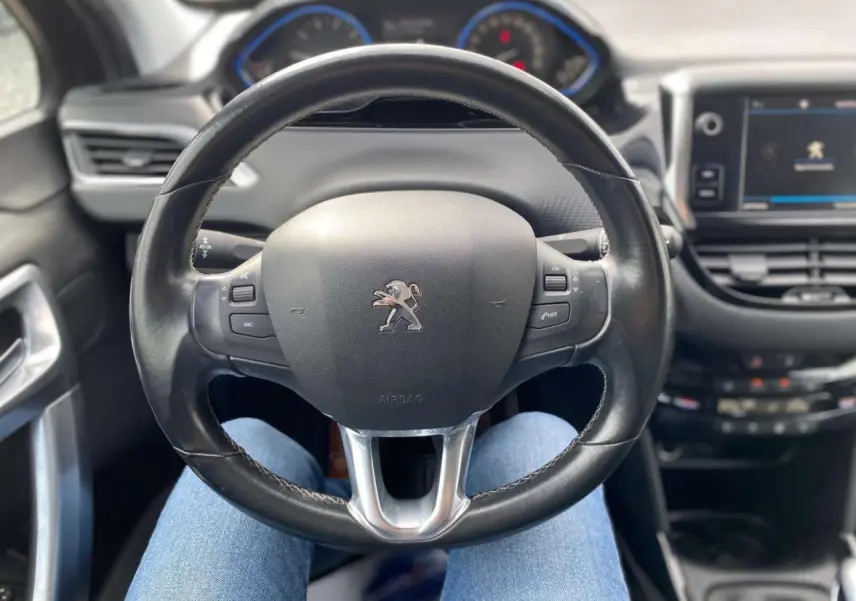 Vue intérieure centrée sur le volant cuir noir du Peugeot 2008 avec tableau de bord et écran tactile en arrière-plan.
