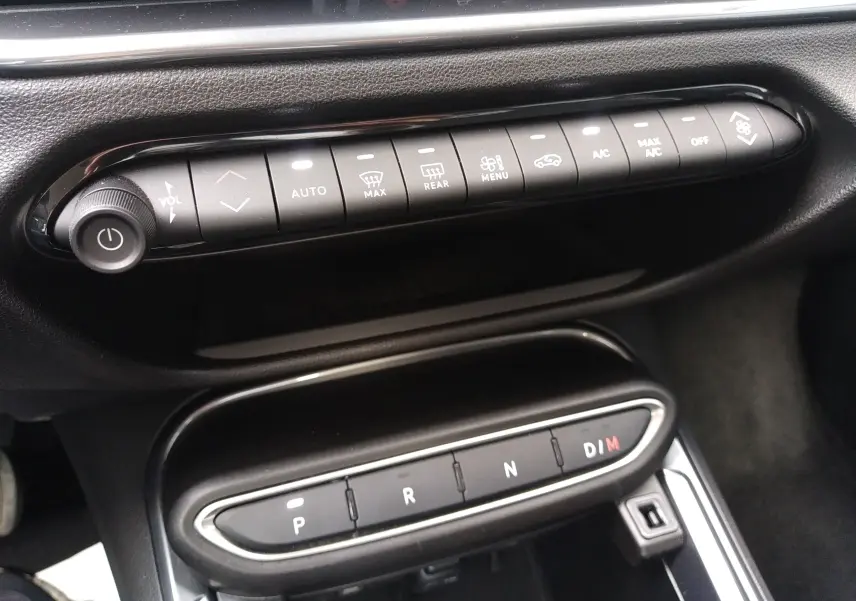 Vue rapprochée de la console centrale noire du Fiat 600 2025, montrant les commandes climatisation et la boîte auto à boutons.
