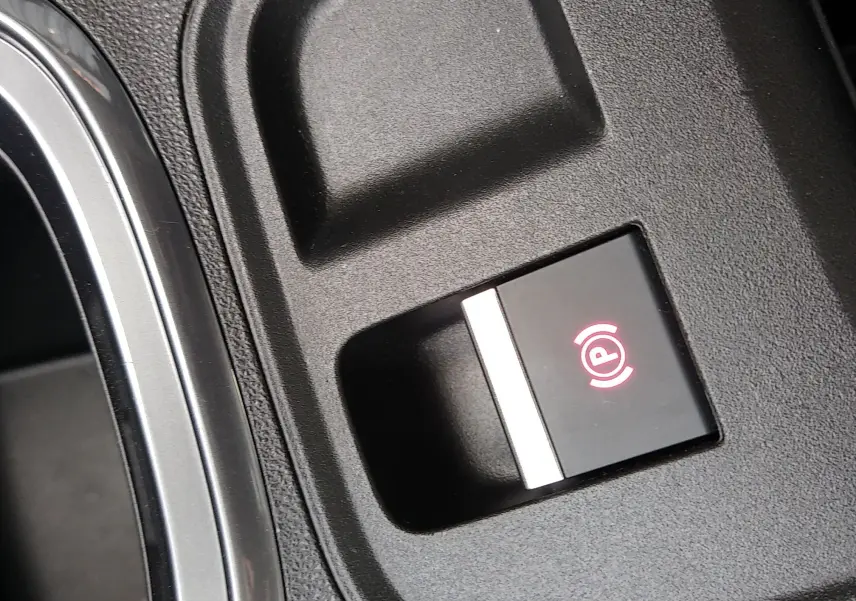Gros plan sur le bouton de frein à main électronique rouge dans l'habitacle noir d'une FIAT 600 hybride 2025.