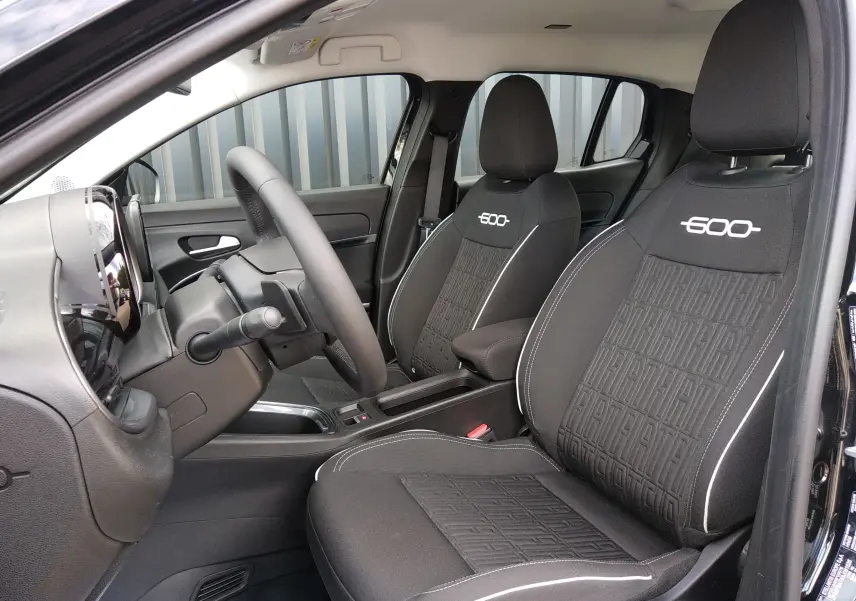 Intérieur de la FIAT 600 hybride 2025 en noir, vue côté conducteur montrant sièges avec logo 600 brodé.