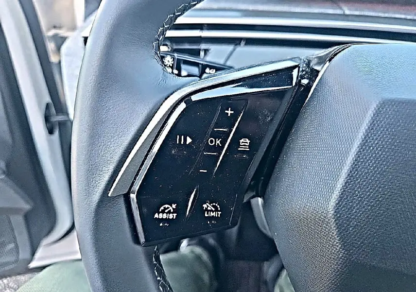 Gros plan sur les commandes noires multifonctions du volant cuir côté gauche du Peugeot 5008 blanc Hybrid 145 allure 2025.