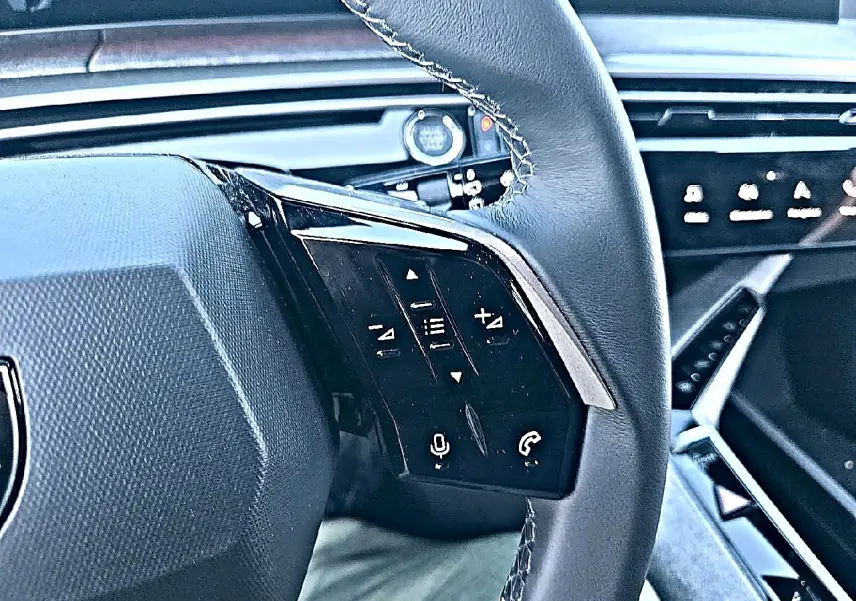 Gros plan sur le volant cuir noir de la Peugeot 5008 Hybrid 145 allure 2025 avec commandes vocales et audio intégrées.
