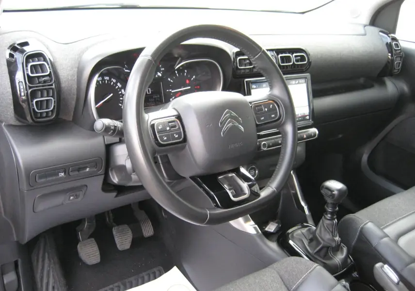 Intérieur du Citroën C3 Aircross gris 2022, vue côté conducteur sur le volant, tableau de bord et levier de vitesses manuel.