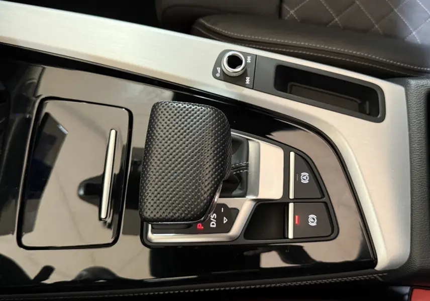 Vue rapprochée de la console centrale avec levier de vitesse noir texturé et finitions aluminium dans une Audi A4 gris foncé.