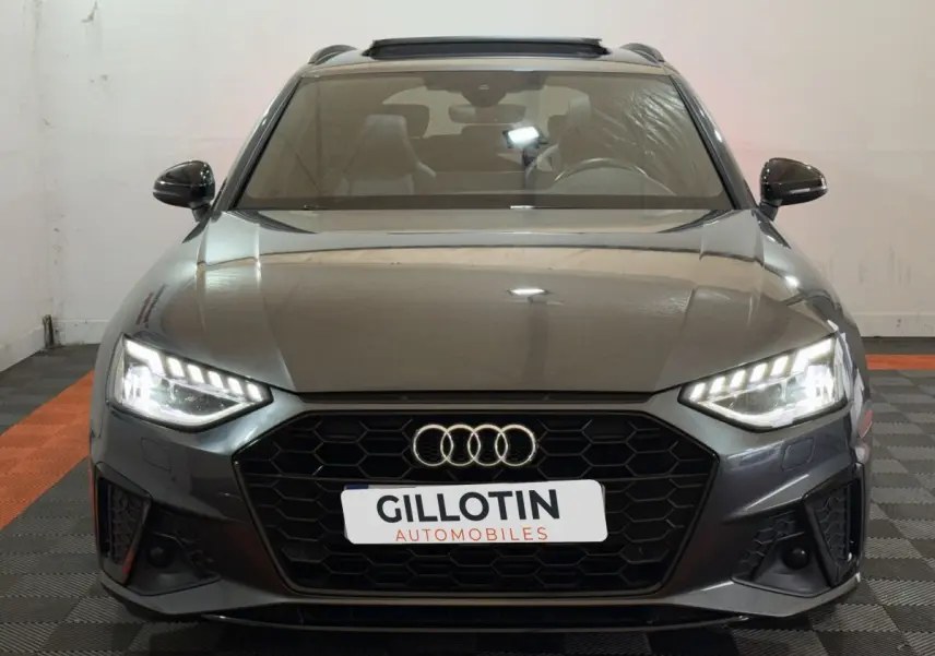 Vue frontale d'une Audi A4 35 TFSI S Edition gris foncé avec phares LED allumés et calandre hexagonale noire.