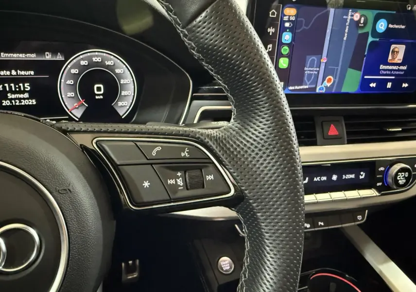 Vue rapprochée de l’intérieur de l’Audi A4 gris foncé, montrant le volant cuir perforé et l’écran tactile central avec navigation.
