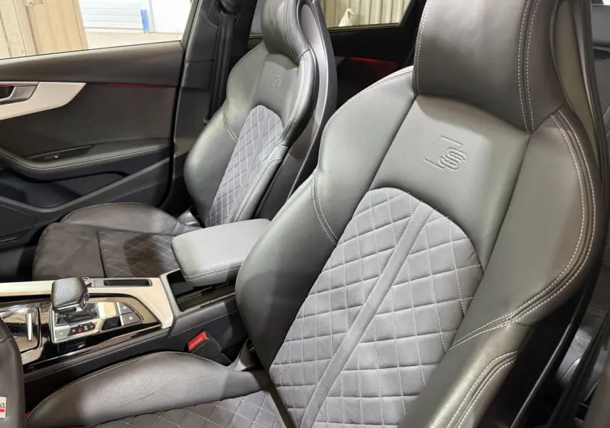 Vue intérieure rapprochée des sièges avant cuir gris foncé avec surpiqûres et logo S sur l’appui-tête de l’Audi A4.