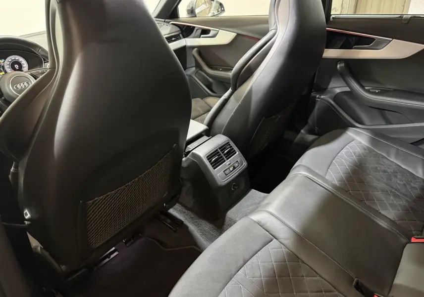 Vue intérieure arrière de l’Audi A4 gris foncé, sièges en cuir noir avec surpiqûres, ventilation arrière et détails rouges d’ambiance.