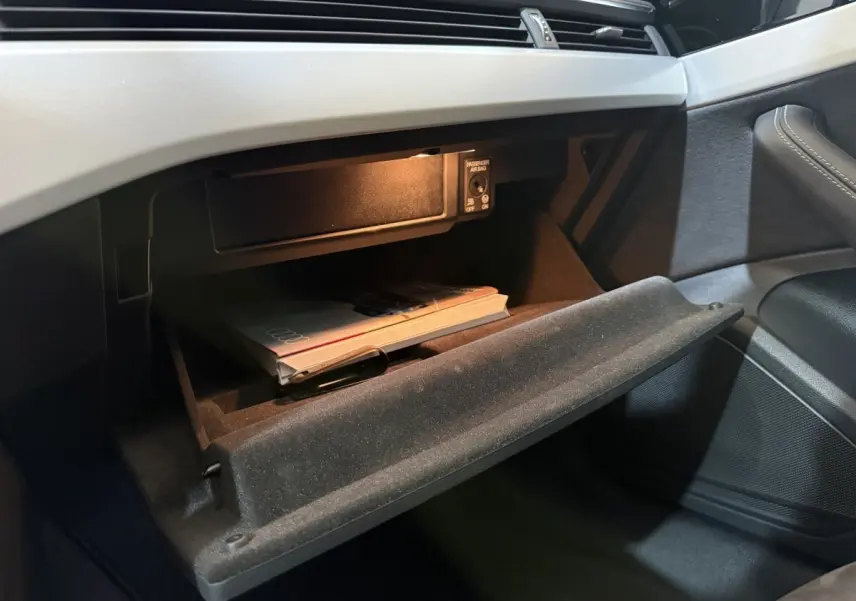 Vue intérieure côté passager de la boîte à gants ouverte avec manuel Audi sur tableau de bord gris clair.