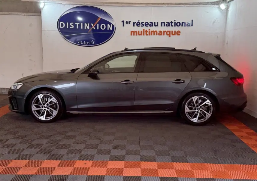 Profil droit d'une Audi A4 35 TFSI S Edition gris foncé en version break, stationnée en intérieur sur sol damier noir et orange.