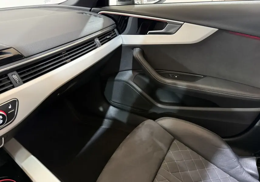 Vue intérieure côté passager de l'Audi A4 gris foncé, mettant en valeur la porte et le siège en cuir avec surpiqûres.