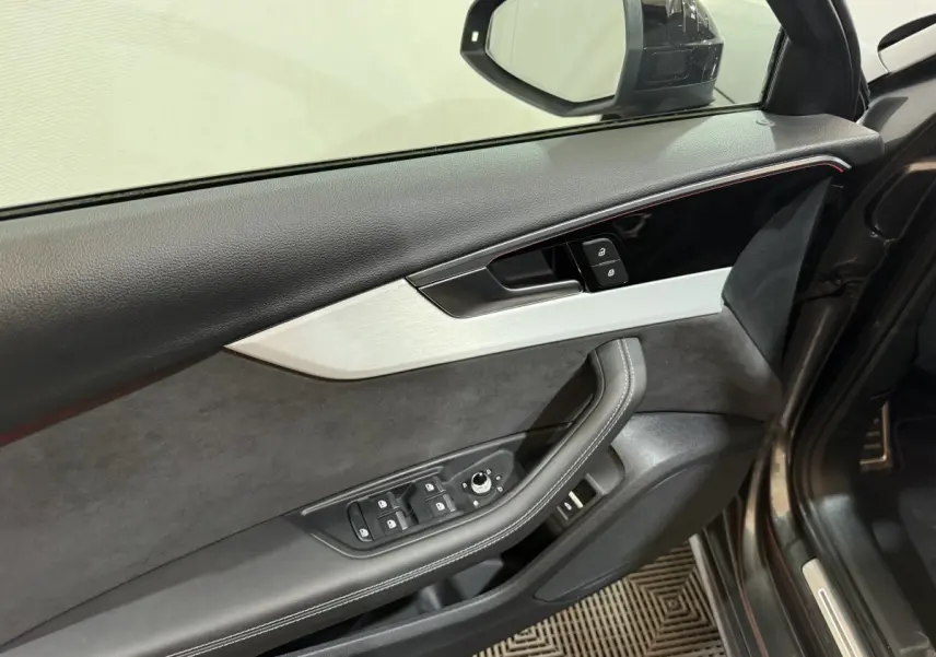 Vue intérieure côté conducteur de la porte d’une Audi A4 gris foncé, avec commandes de vitres et rétroviseur intégrées.