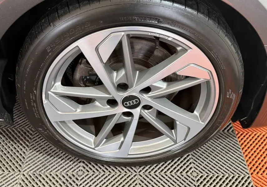 Gros plan sur la jante en alliage argentée Audi Sport d'une Audi A4 gris foncé, roue avant droite visible.