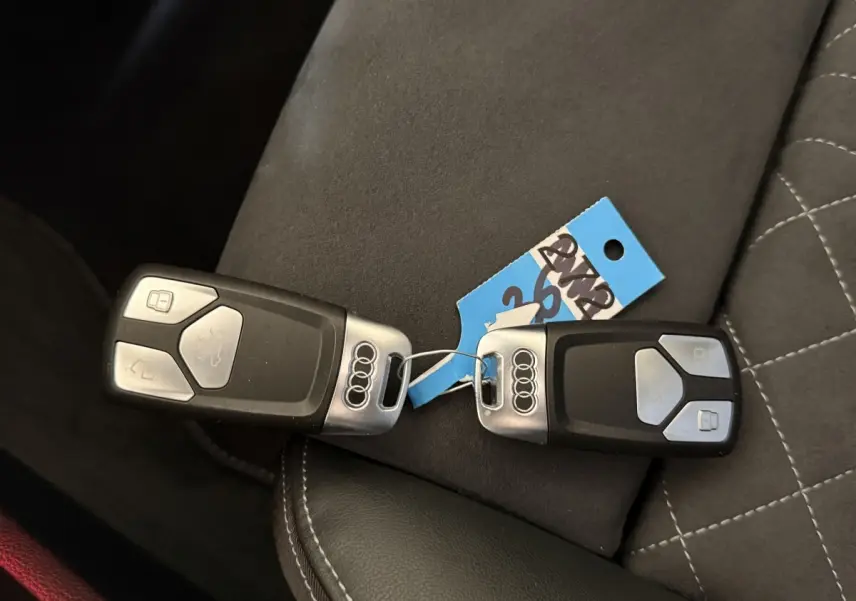 Gros plan sur deux clés Audi noires avec logo argent posées sur un siège en cuir noir et tissu gris.