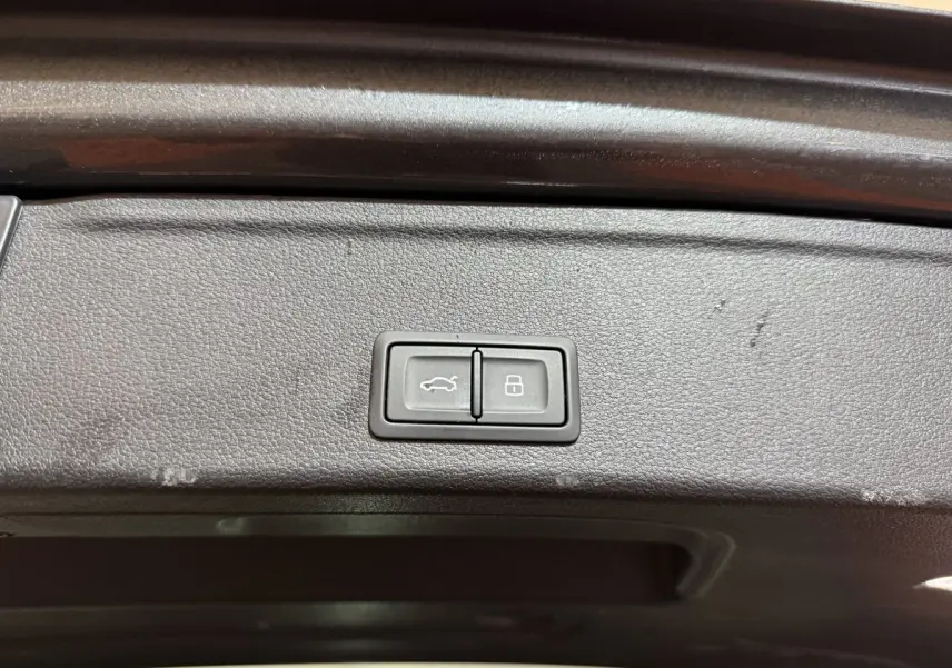 Boutons d'ouverture et de verrouillage du coffre sur le panneau intérieur du hayon d'une Audi A4 gris foncé, vue rapprochée.