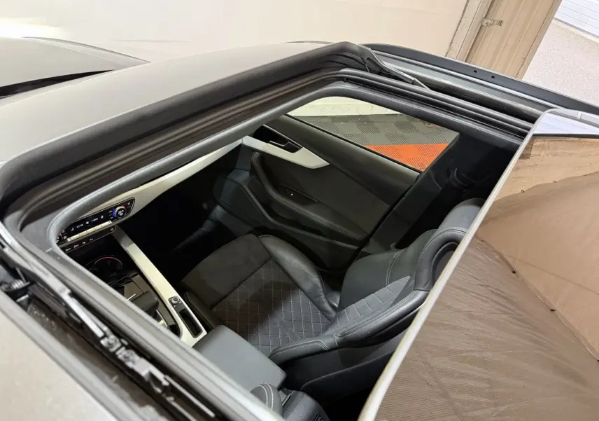 Vue intérieure par le toit ouvrant d'une Audi A4 gris foncé, montrant le siège avant droit et la console centrale.