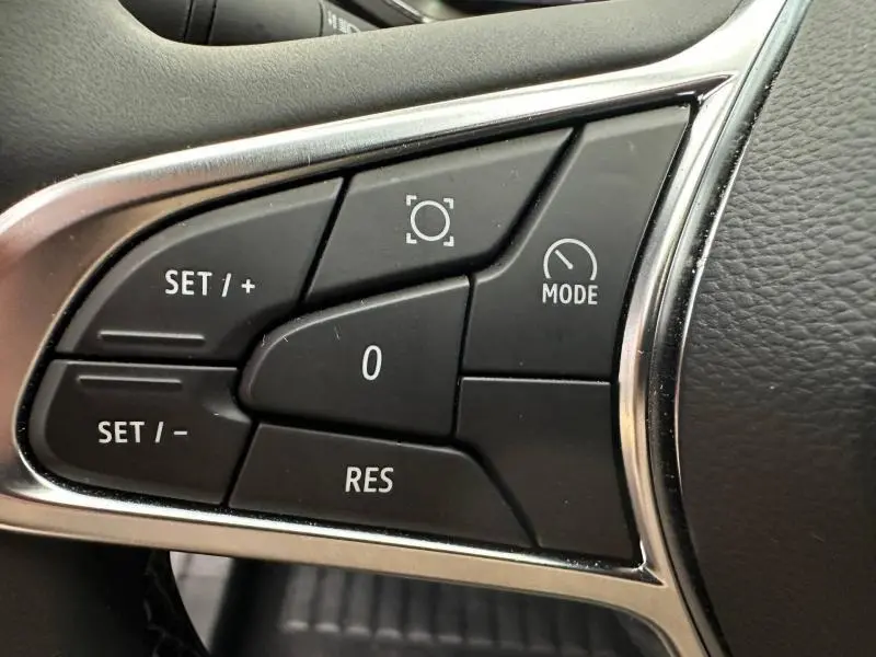 Gros plan sur les commandes noires du volant du Renault Captur 2025, avec boutons de réglage et mode, entouré de finition chrome.