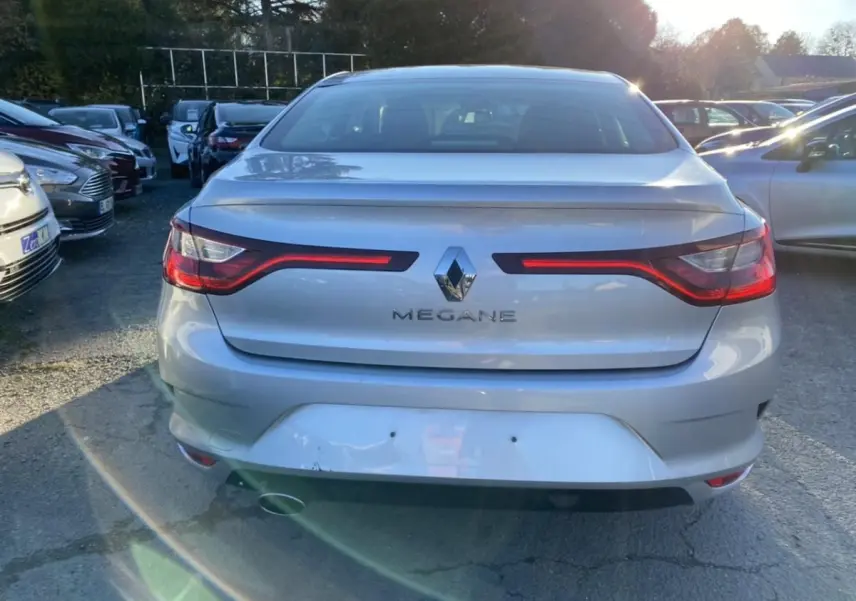 Vue arrière d'une Renault Mégane Sedan gris platine de 2017, avec feux arrière allumés et logo central visible.