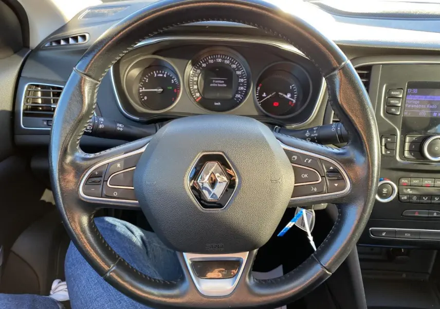 Vue rapprochée du volant en cuir noir de la Renault Mégane gris platine, avec tableau de bord et console centrale visibles.