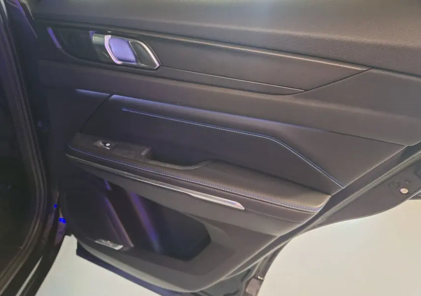 Vue rapprochée de la porte arrière gauche noire du LYNK & CO 01 2023 avec surpiqûres bleues et poignée argentée.