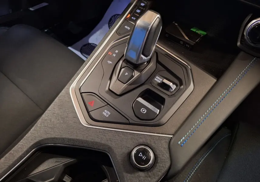 Gros plan sur la console centrale noire du Lynk & Co 01 2023, mettant en valeur le levier de vitesses et les surpiqûres bleues.