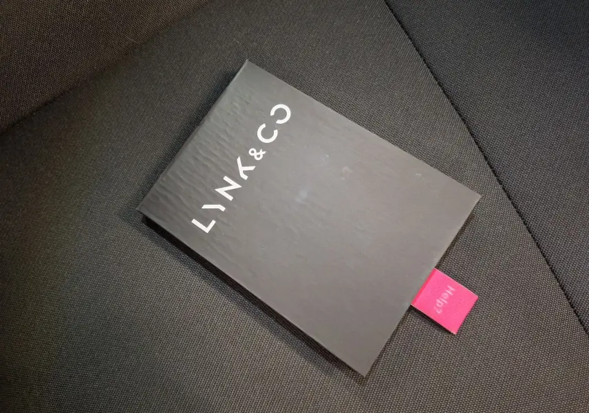 Manuel d'utilisation noir Lynk & Co posé sur un siège en tissu gris foncé, vue en plongée rapprochée.