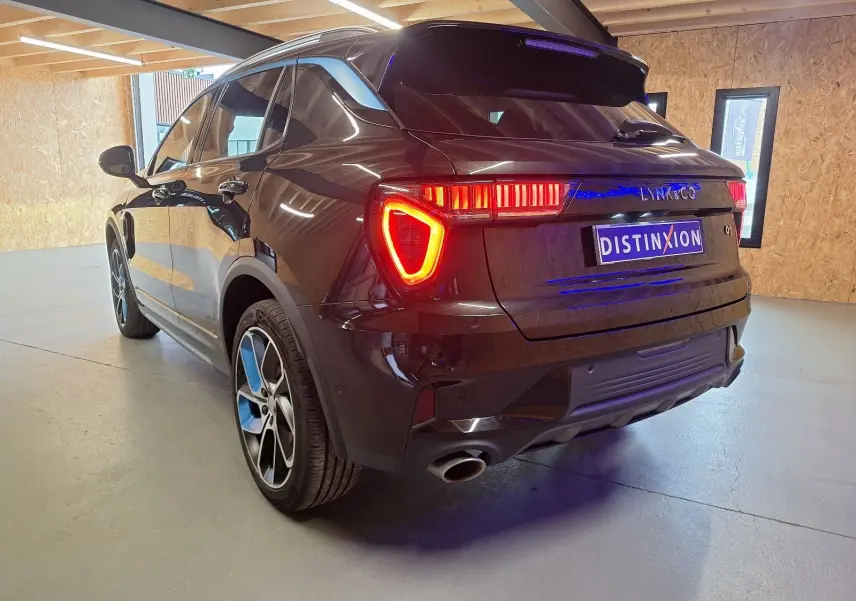 Vue 3/4 arrière droite d'un SUV LYNK & CO 01 noir avec feux arrière allumés dans un intérieur clair.