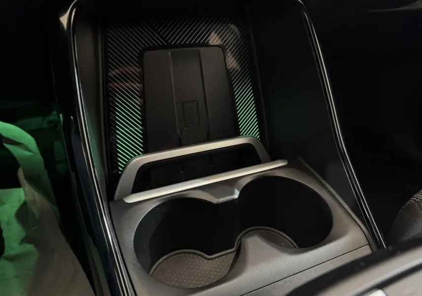 Gros plan sur la console centrale noire du BMW X1 2024 avec porte-gobelets et zone de recharge à induction éclairée.