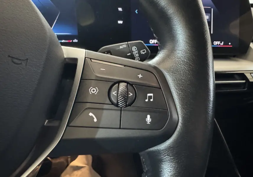 Gros plan sur le volant cuir noir du BMW X1 2024, côté gauche, avec commandes audio et vocales visibles.