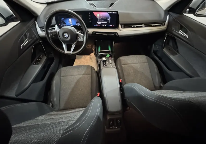 Vue intérieure avant du BMW X1 2024 gris foncé, avec tableau de bord digital et sièges tissu gris.