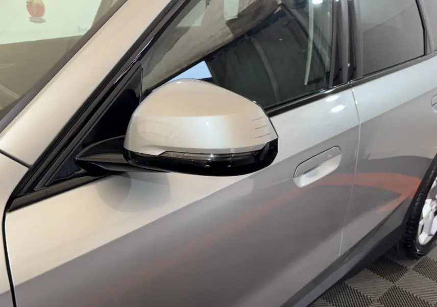 Gros plan sur le rétroviseur côté conducteur gris clair du BMW X1 sDrive20i 2024, avec porte et poignée visibles.