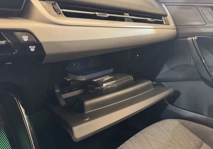 Vue intérieure côté passager du BMW X1 2024 gris foncé, boîte à gants ouverte avec objets rangés visibles.