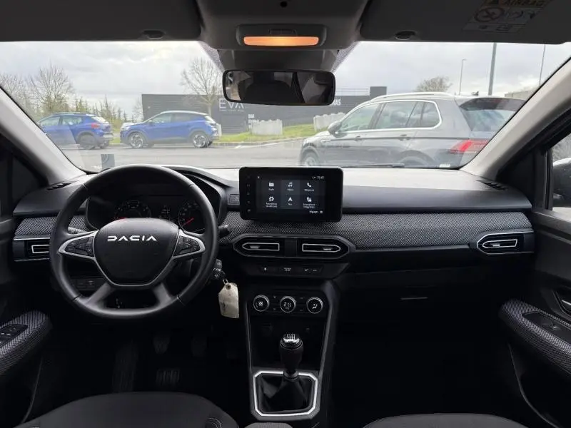 Vue intérieure frontale du tableau de bord du Dacia Jogger 2025, avec volant, écran tactile et levier de vitesses manuel.