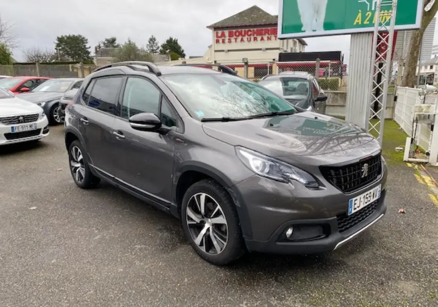 Peugeot 2008 gris platinium en 3/4 avant droit, avec jantes alliage 17 pouces noir brillant et barres de toit noires.