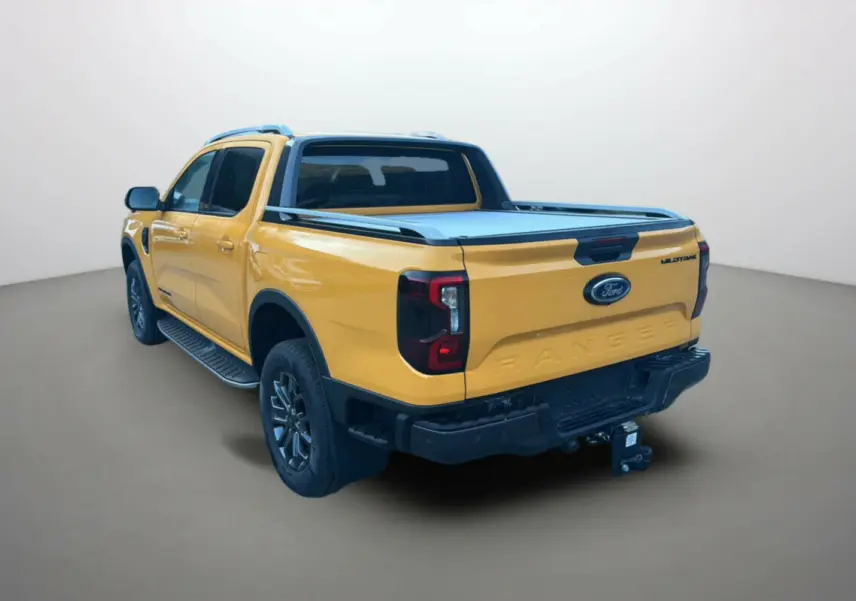 Ford Ranger 2.3 PHEV Wildtrak Plus 2026 en Cyber orange, vue 3/4 arrière droite avec attelage et barres de toit.
