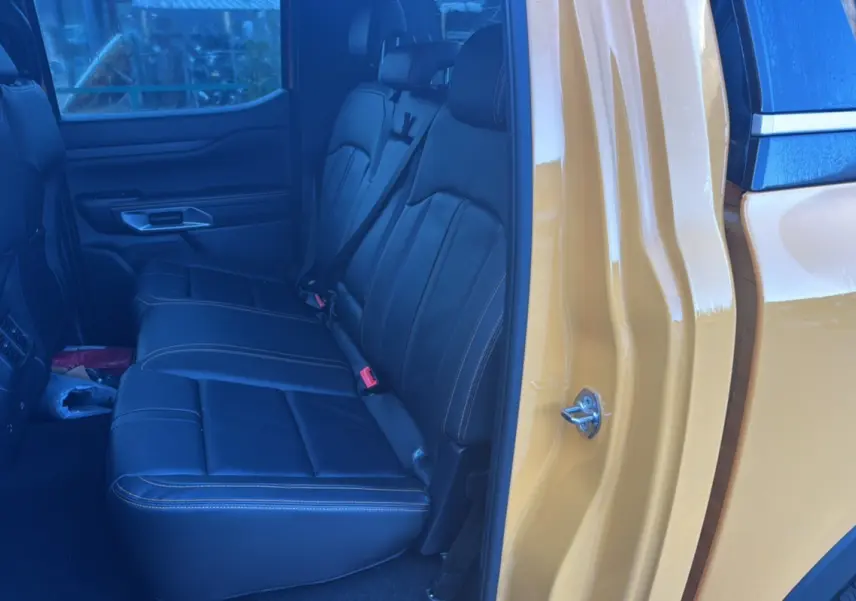Vue intérieure arrière côté droit du Ford Ranger Cyber orange, montrant les sièges en cuir noir avec surpiqûres contrastantes.