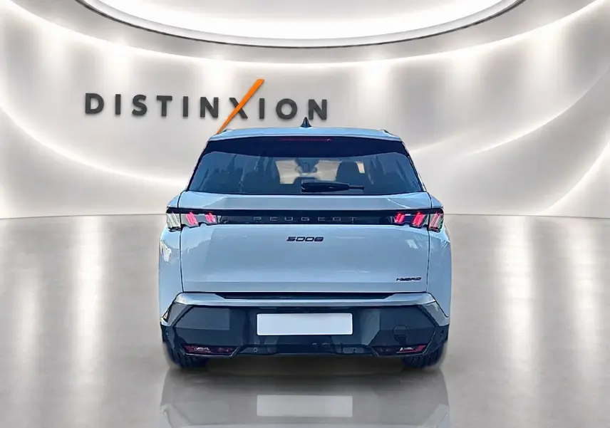 Vue arrière d’un Peugeot 5008 blanc hybride 2025 avec feux LED et becquet arrière dans un showroom lumineux.