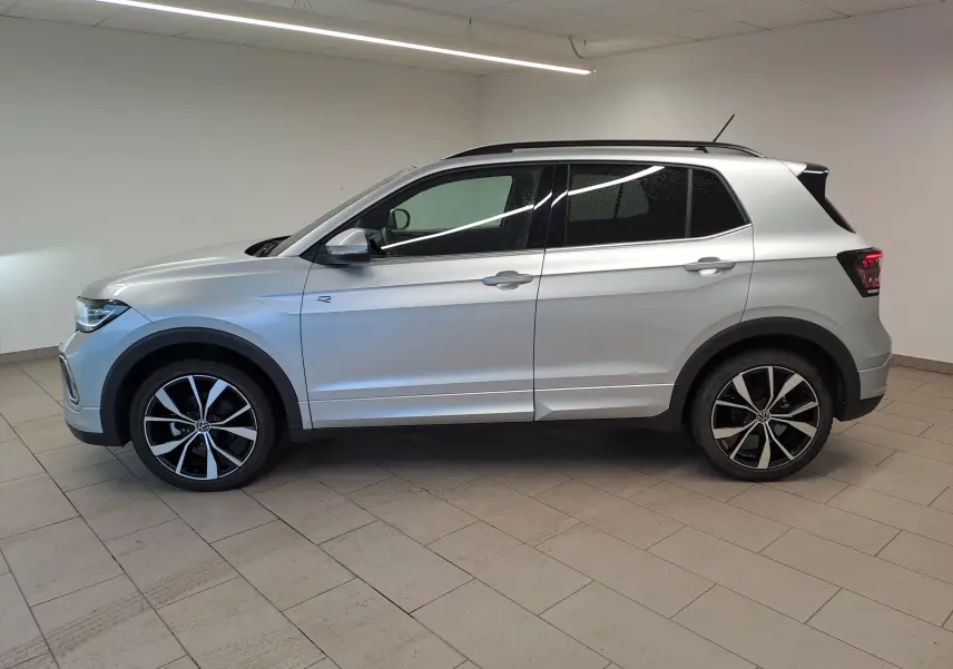 Vue de profil côté gauche d'un Volkswagen T-Cross 2025 argent Reflet, version R-Line avec jantes noires et argentées.