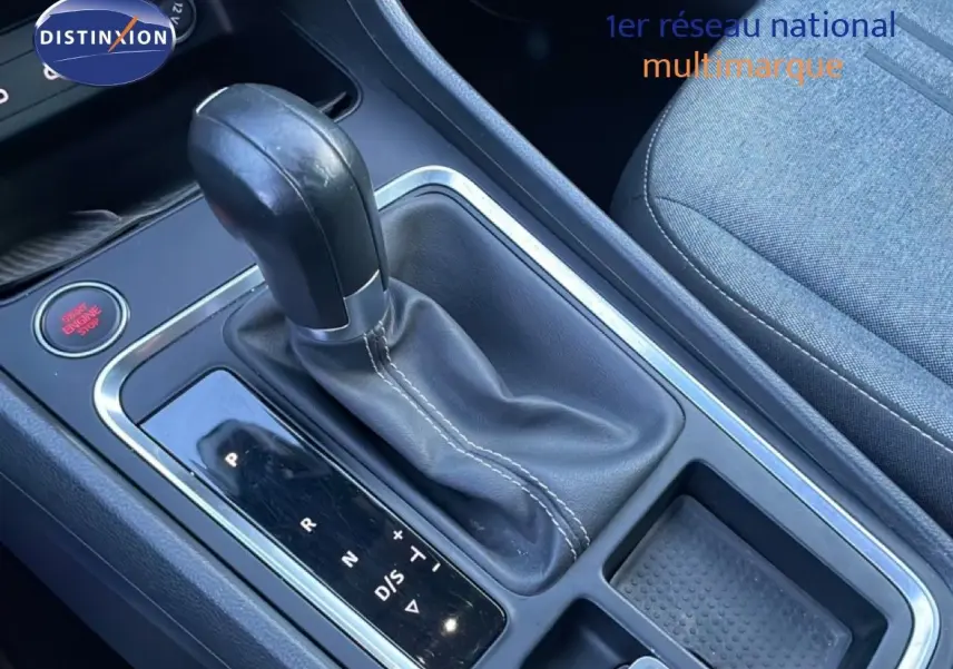 Gros plan sur la console centrale avec levier de vitesse automatique en cuir noir et siège tissu gris à droite.