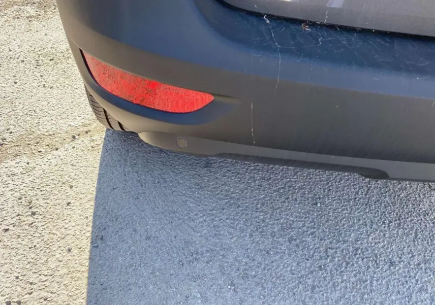 Gros plan sur le pare-chocs arrière gris platinium métallisé du Peugeot 5008 avec feu rouge et capteur de stationnement.