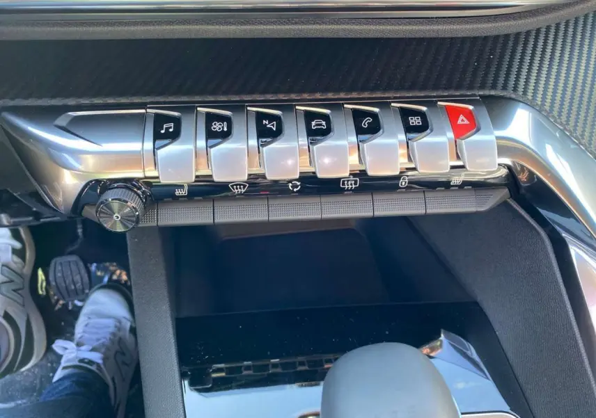 Gros plan sur la rangée de boutons chromés du tableau de bord du Peugeot 5008, avec molette et levier de vitesses visible.